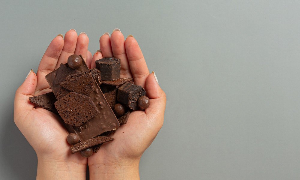 Manos femeninas sosteniendo una selección de chocolates artesanos con texturas y matices variados.